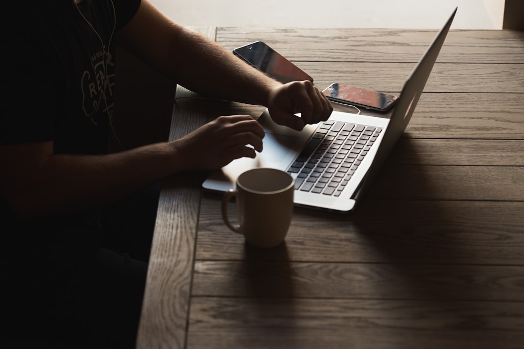 Gray laptop computer on brown wooden table beside person sitting on chair